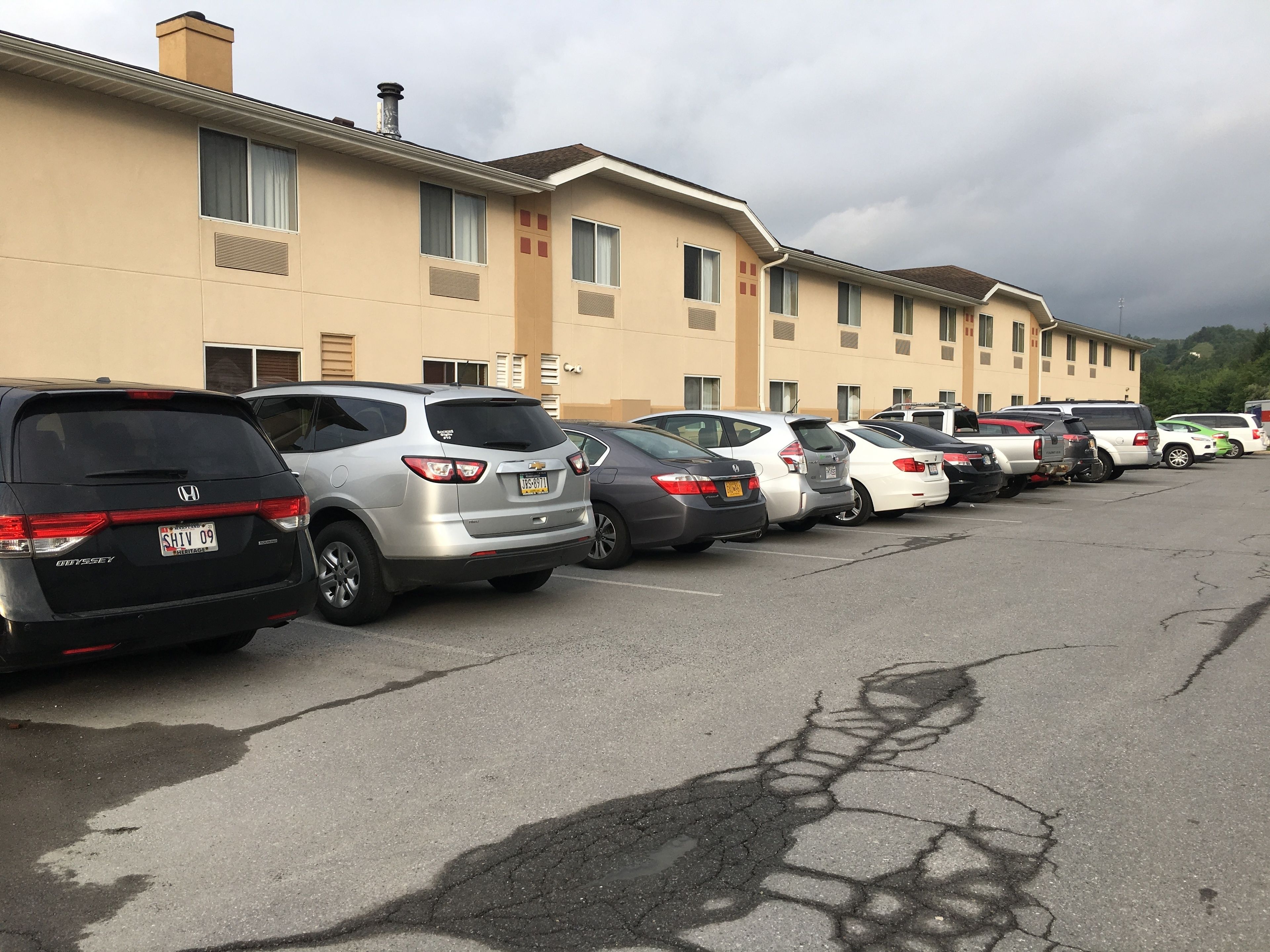 Un estacionamiento con varios coches aparcados frente a un edificio de fachada color crema y numerosas ventanas.