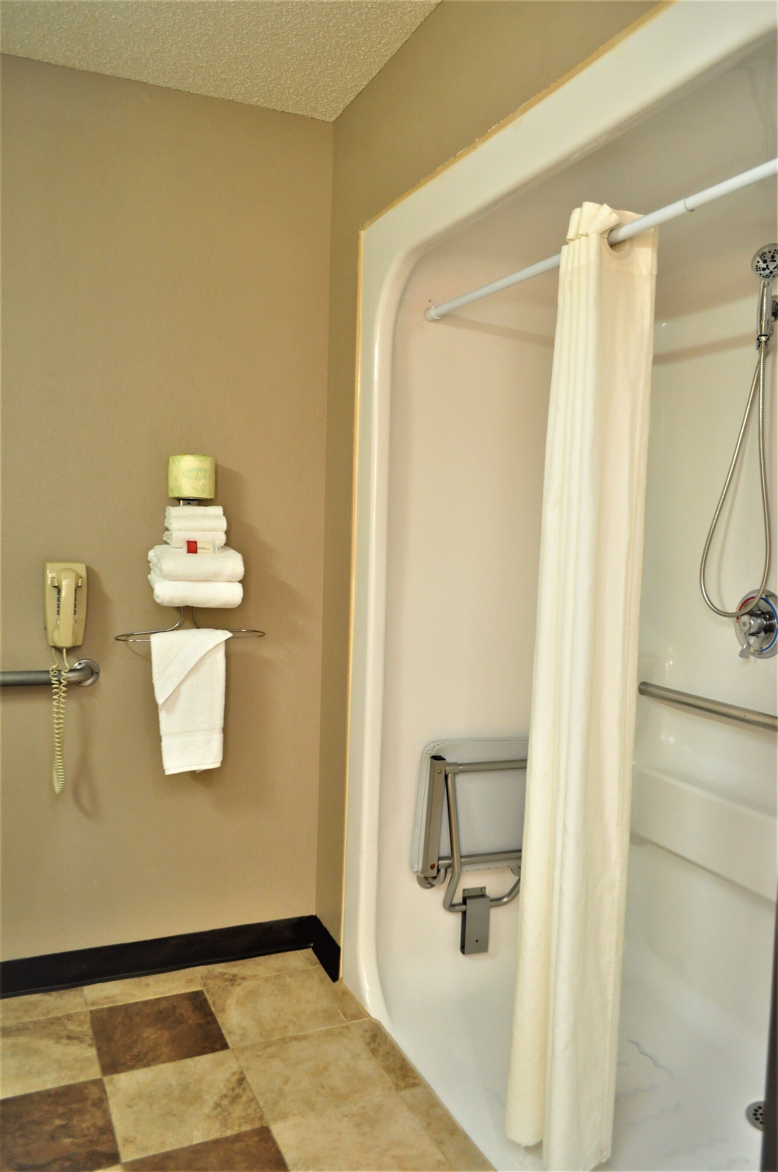 A bathroom with a bathtub, a shower, a towel rack with towels, and a telephone.