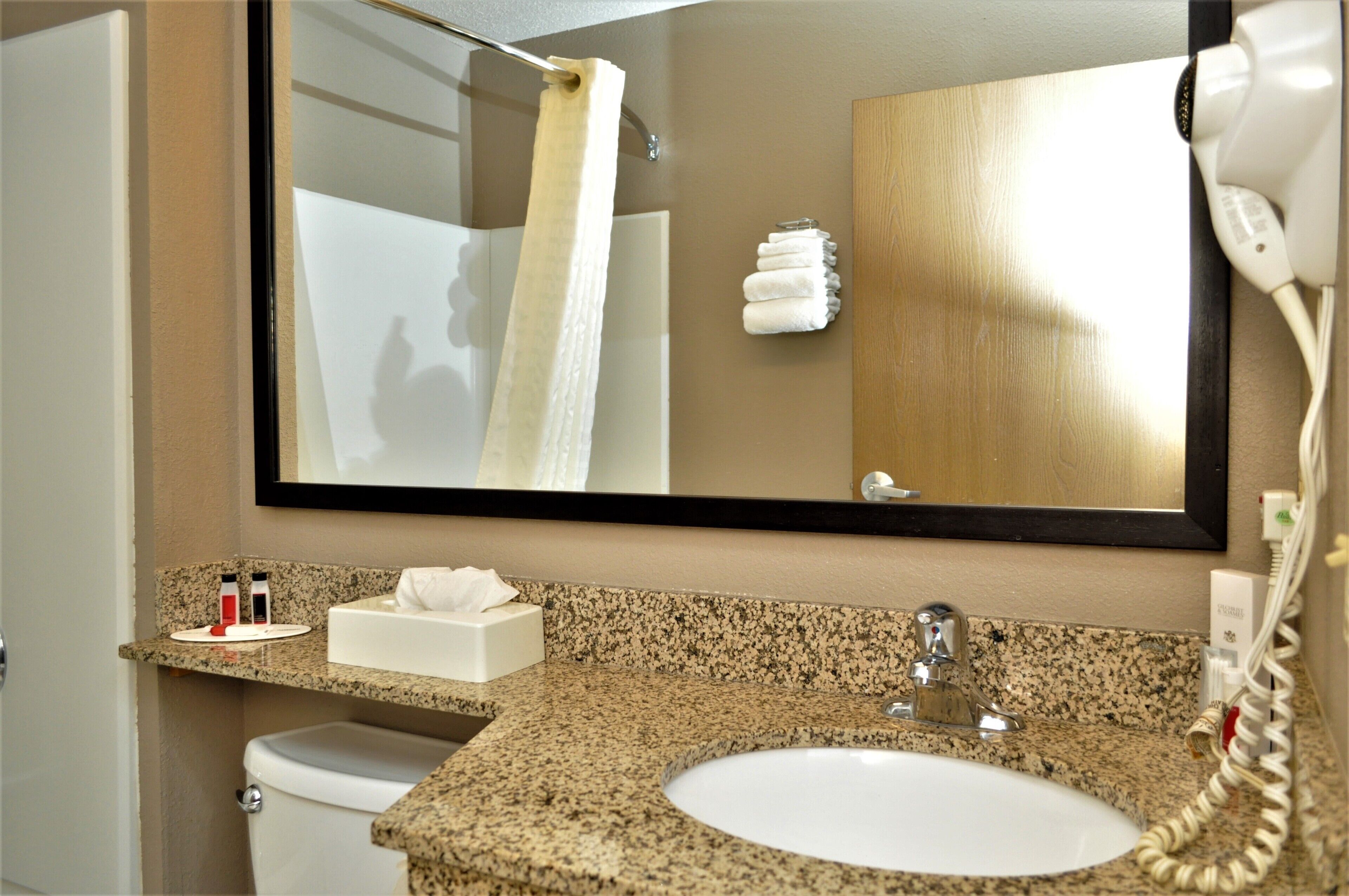 A bathroom with a granite countertop, a white sink, a mirror, a towel rack, and a hairdryer.