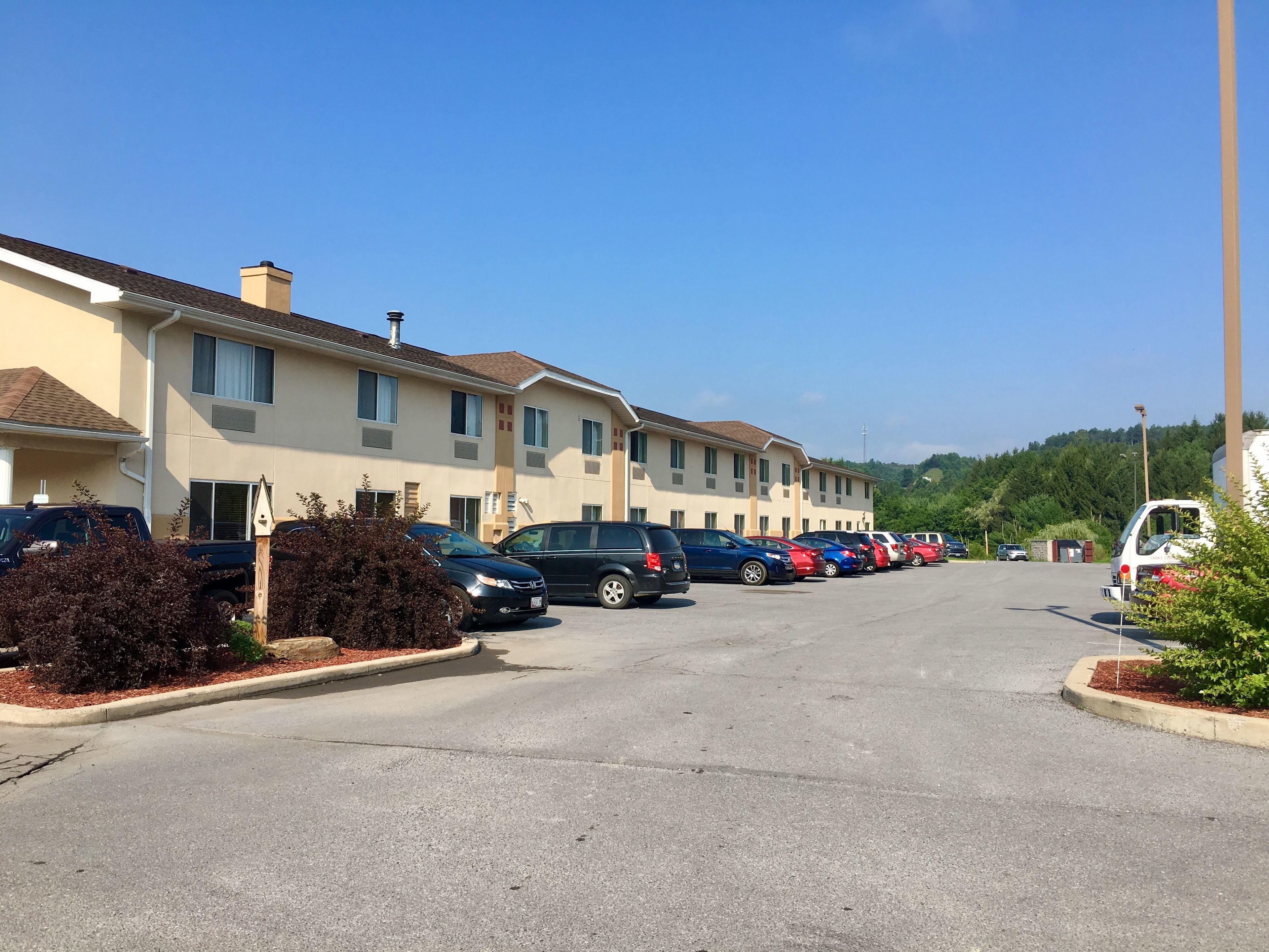 Un parking rempli de voitures et une rangée de bâtiments à deux étages, dotés de grandes fenêtres et d’un toit plat.