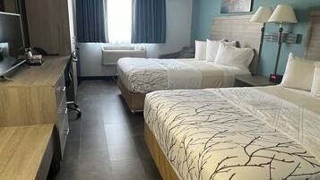 A hotel room with two beds, a desk, a chair, a TV, and a window with curtains.