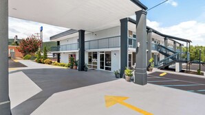 A hotel entrance with a covered walkway, potted plants, and a clear sky. - Rodeway Inn Dalton South (Dalton)