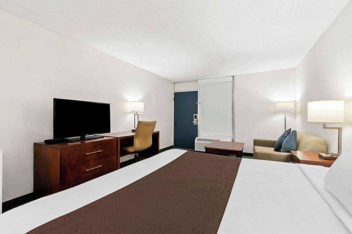 Hotellihuone, jossa on sänky, televisio, työpöytä tuolilla, sohva ja lamppu.