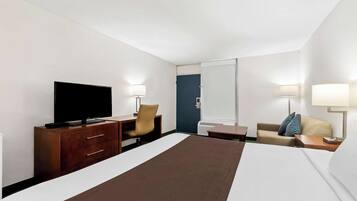 A hotel room with a bed, a TV, a desk with a chair, a sofa, and a lamp.
