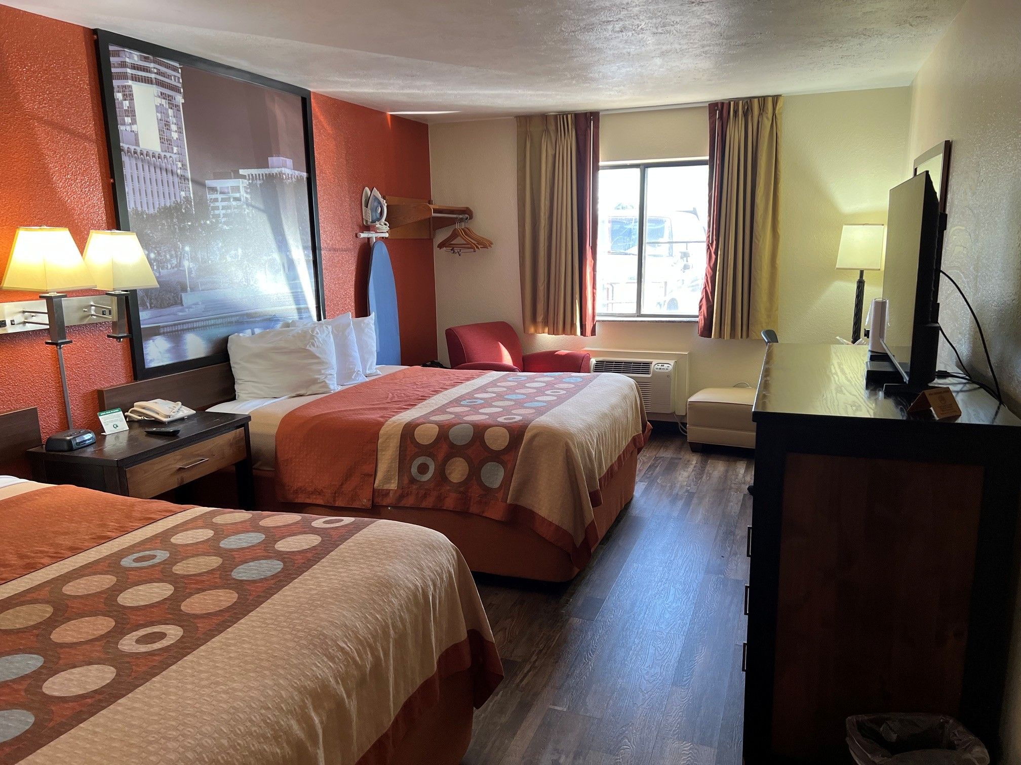 A hotel room with two beds, a desk, a TV, and a window with curtains.