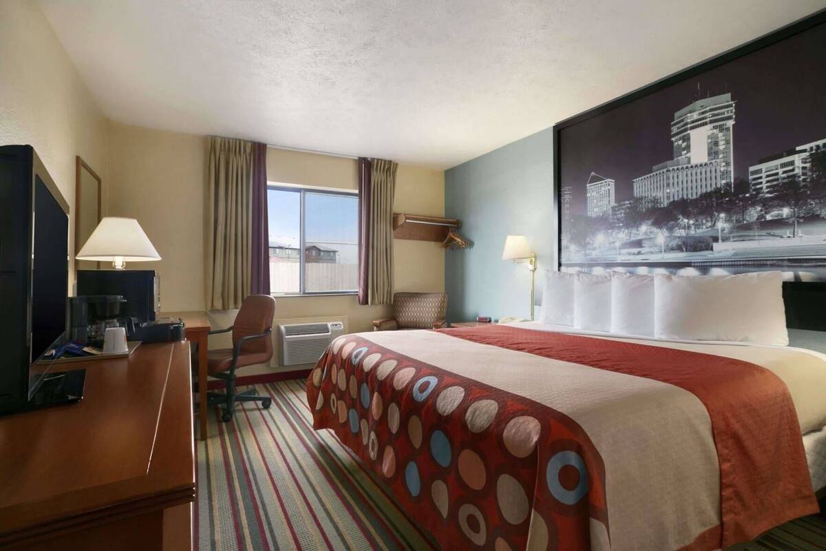 Habitación de hotel con cama, escritorio, silla y un amplio ventanal.