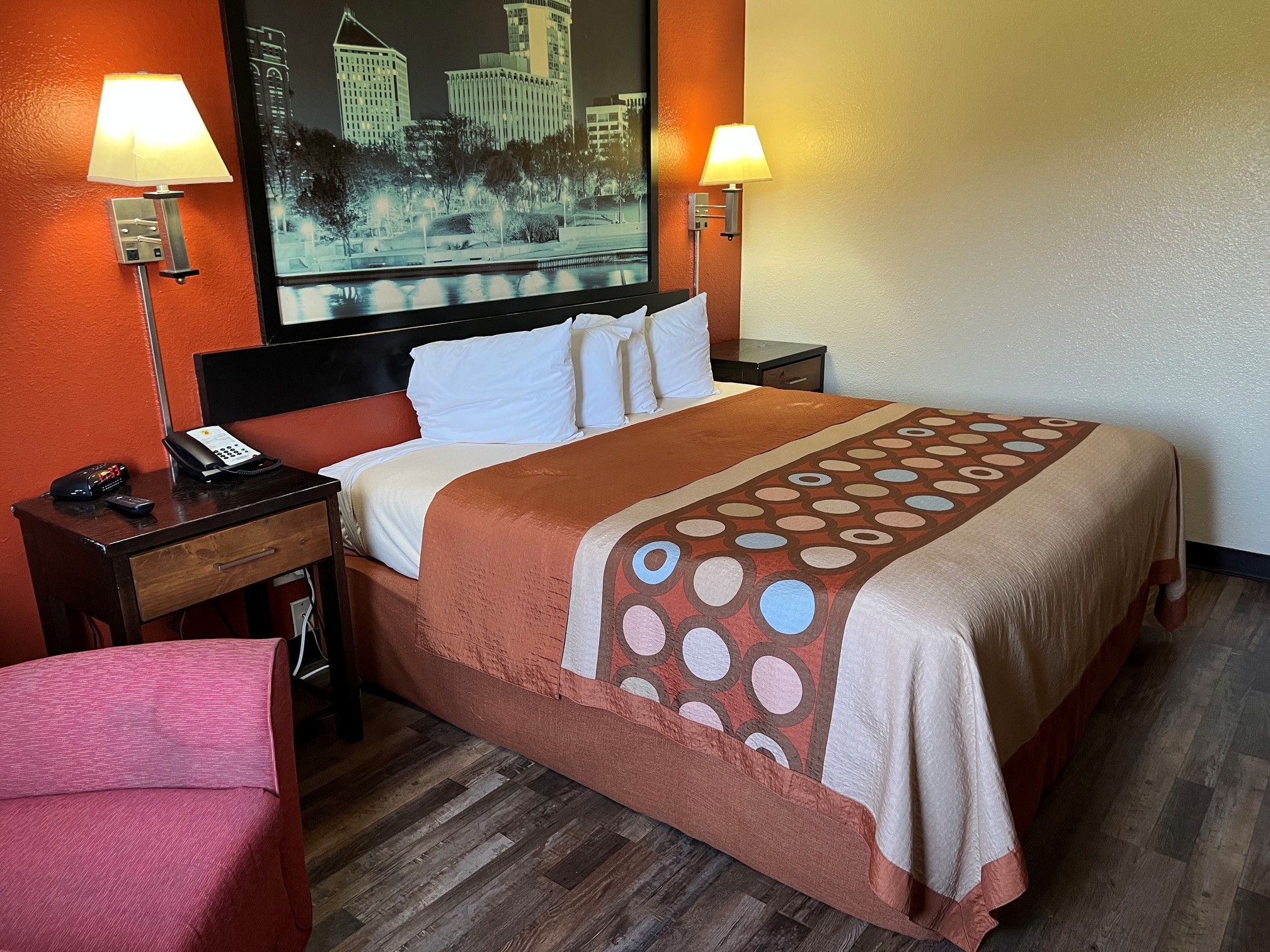 A hotel room with a bed, two bedside tables, a chair, a painting on the wall, and a wooden floor.