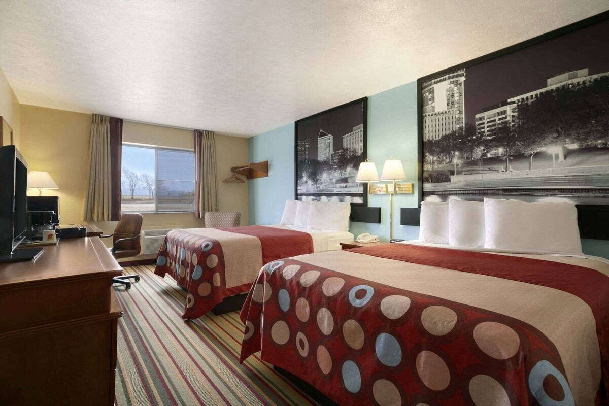 Habitación de hotel con dos camas, un escritorio, una silla, un televisor y una ventana con cortinas.
