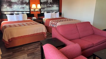 A hotel room with two beds, a red sofa, a small table, and a nightstand with a lamp.