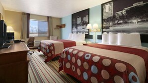 Quarto de hotel com duas camas, uma mesa de trabalho, uma cadeira, uma televisão e uma janela com cortinas.