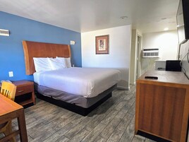 A hotel room with a bed, a desk, a chair, and a picture on the wall.