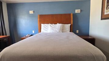 A hotel room with a large bed, wooden headboard, white pillows, and bedside tables with a phone and a light switch.