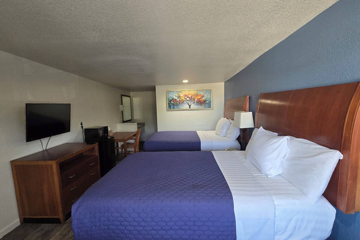 A hotel room with two beds, a desk, a television, and a painting on the wall.