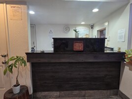 A reception desk with a sign indicating check-in times, a clock, and a 'Welcome to Peach City Inn' sign.