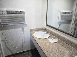 A bathroom with a white sink, a mirror, and a wall-mounted air conditioner.