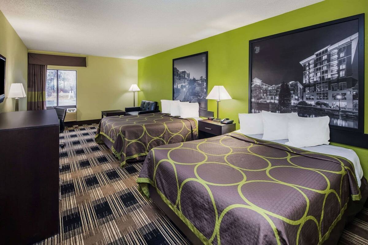 Une chambre d’hôtel avec deux lits, un bureau, une chaise, une fenêtre avec des rideaux et deux lampes.