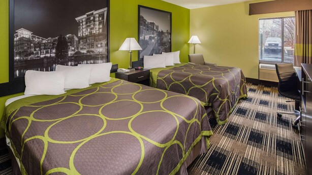 Une chambre d’hôtel avec deux lits, des murs verts et de grandes affiches en noir et blanc représentant des paysages urbains.