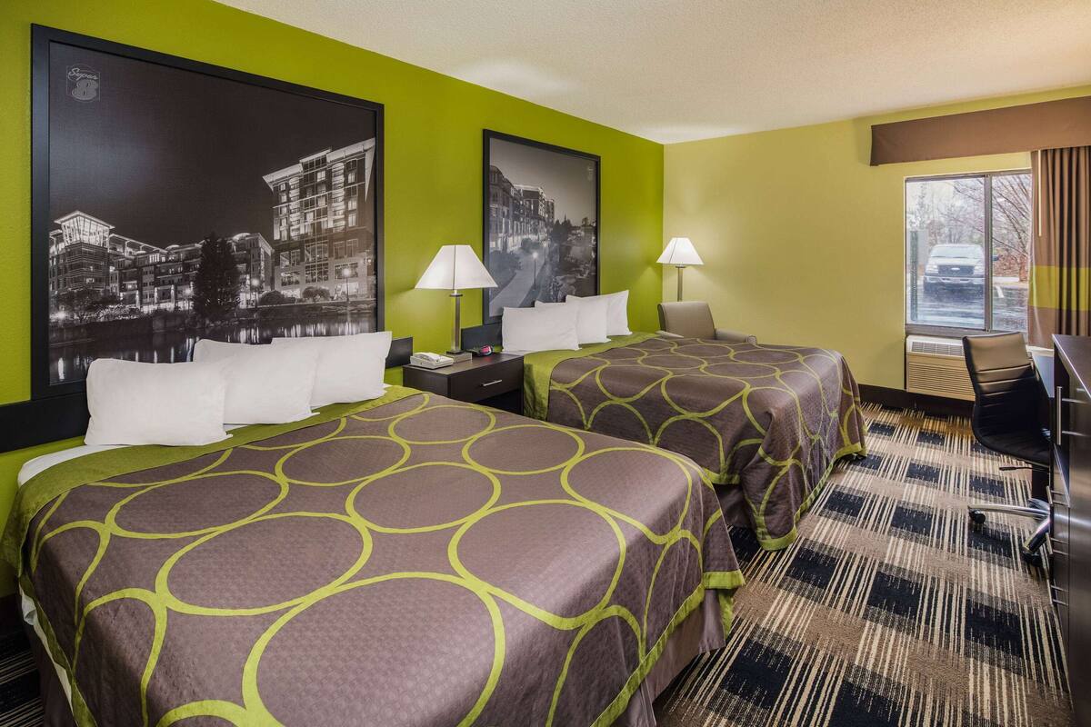 Une chambre d’hôtel avec deux lits, des murs verts et de grandes affiches en noir et blanc représentant des paysages urbains.