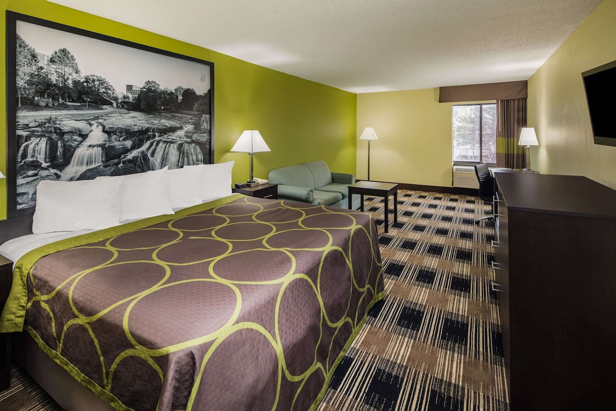 Une chambre d’hôtel avec un grand lit, un bureau, une chaise, deux lampes et un grand tableau encadré représentant une cascade.