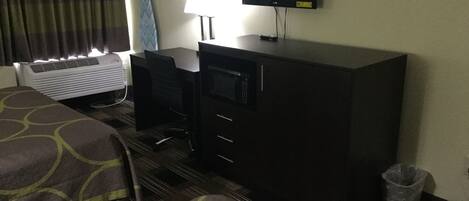A hotel room with two beds, a desk, a television, and an air conditioning unit.