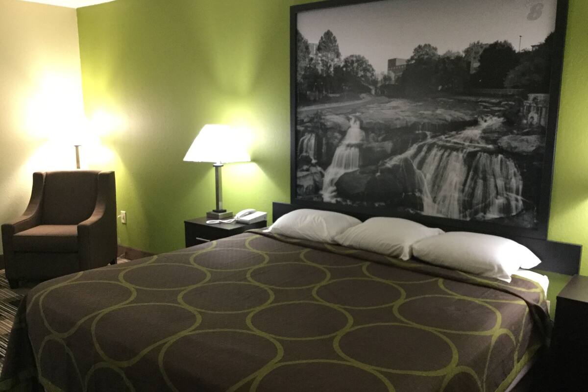 Une chambre d’hôtel avec un lit, une chaise, une table de chevet avec une lampe et un grand tableau encadré représentant une cascade.