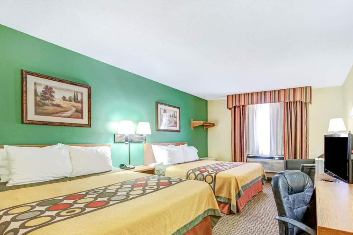 Une chambre d’hôtel avec deux lits, un bureau avec une chaise, une télévision et deux tableaux encadrés au mur.