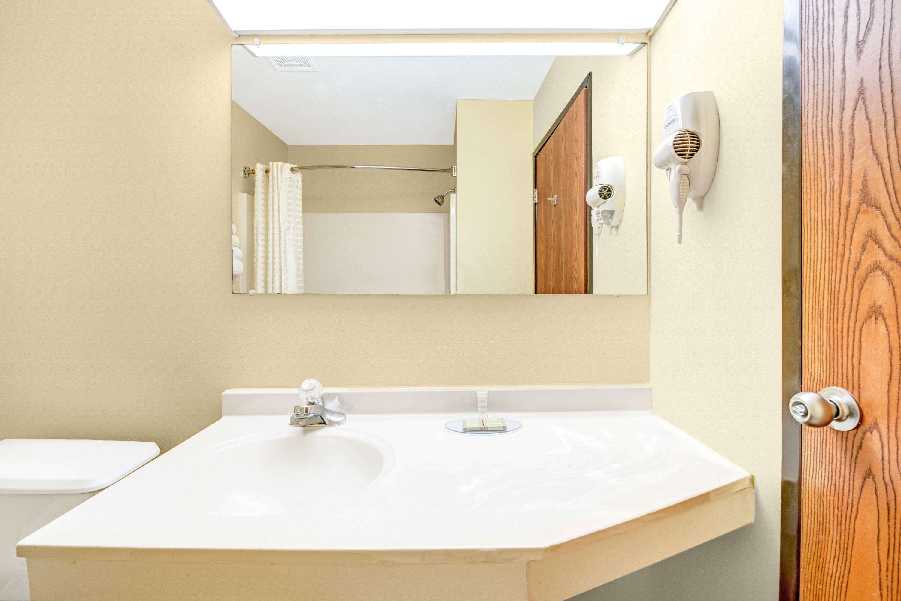 A bathroom with a white sink, a mirror, a towel rack, and a hairdryer on the wall.