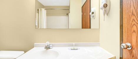 A bathroom with a white sink, a mirror, a towel rack, and a hairdryer on the wall.
