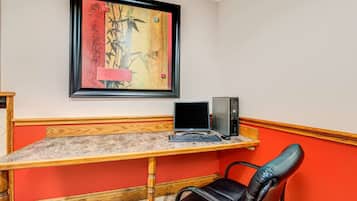 Una habitación con un escritorio de madera, una computadora, una silla y una obra de arte enmarcada en la pared.
