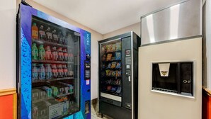 Un espace comprenant un distributeur automatique aux couleurs bleu et violet, doté d’un bouton-poussoir et d’un réfrigérateur en acier inoxydable.