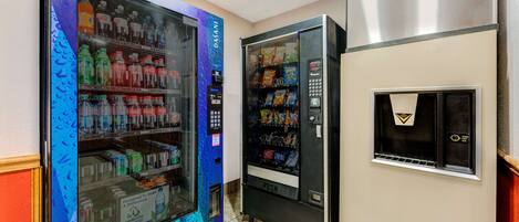 A vending machine area with a blue and purple design, a push button, and a stainless steel refrigerator.