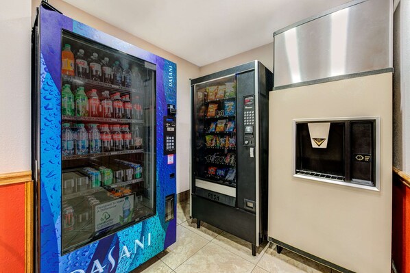 A vending machine area with a blue and purple design, a push button, and a stainless steel refrigerator.