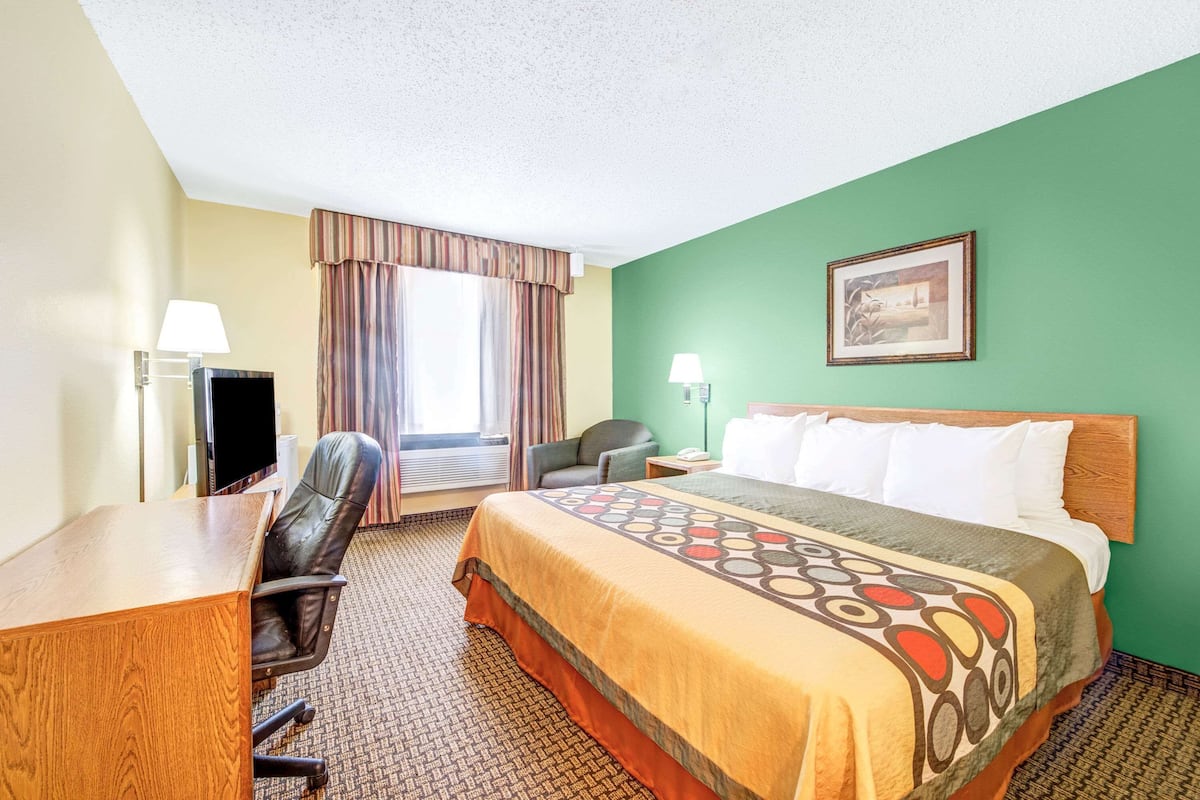 Une chambre d’hôtel avec un lit, un bureau, une chaise, une lampe et un tableau au mur.