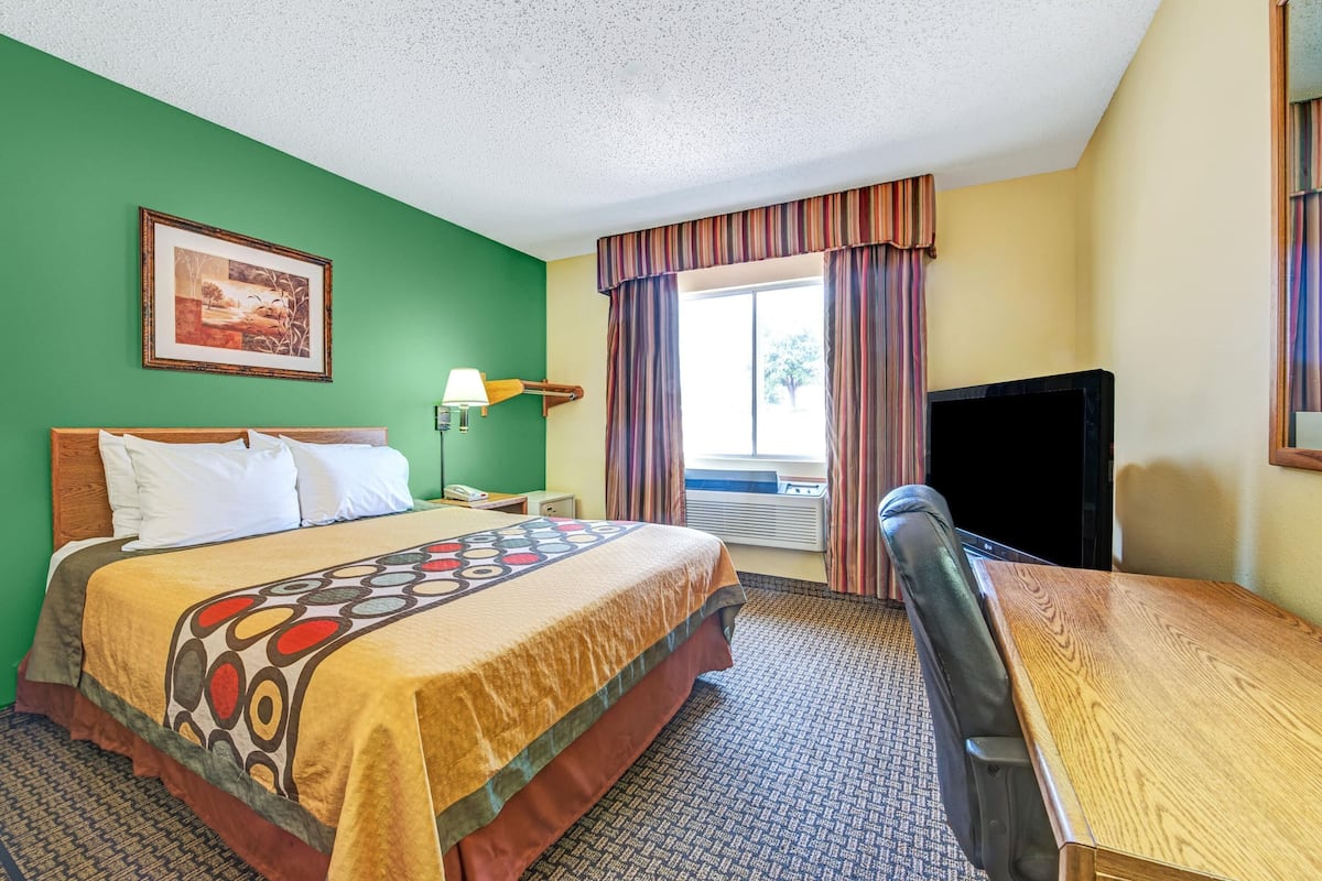 Une chambre d’hôtel équipée d’un lit, d’un bureau, d’une chaise, d’une télévision, d’une lampe et d’une fenêtre avec des rideaux.