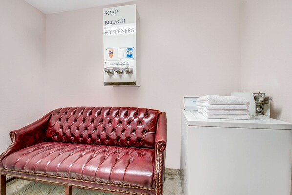 A room with a red leather sofa, a white washing machine, and a soap dispenser on the wall.