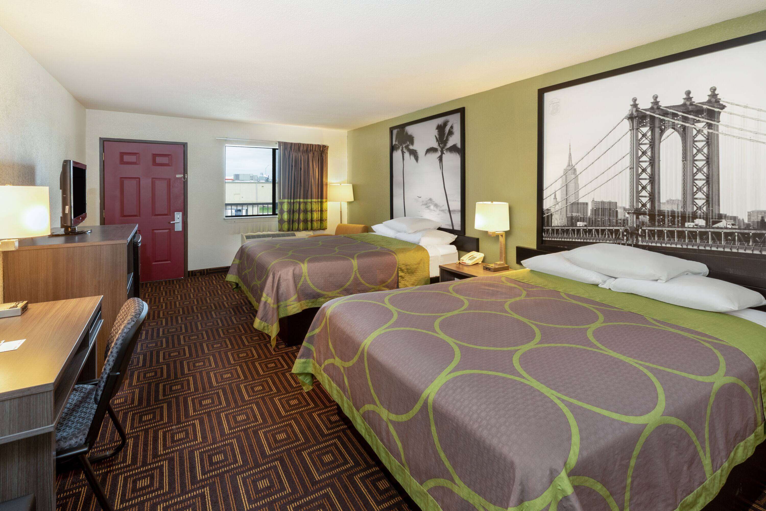 A hotel room with two beds, a desk, a TV, and a large window.
