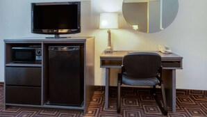 Une chambre d’hôtel équipée d’une télévision à écran plat, d’un bureau avec une lampe, d’une chaise, d’un four à micro-ondes et d’un réfrigérateur.