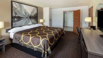 Habitación de hotel con una cama grande, un escritorio, una silla, un televisor y un baño visible a través de una puerta abierta.