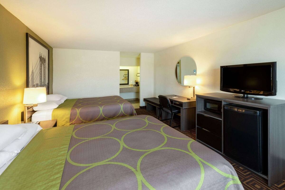 Ein Hotelzimmer mit zwei Betten, einem Schreibtisch, einem Fernseher und einem Spiegel.