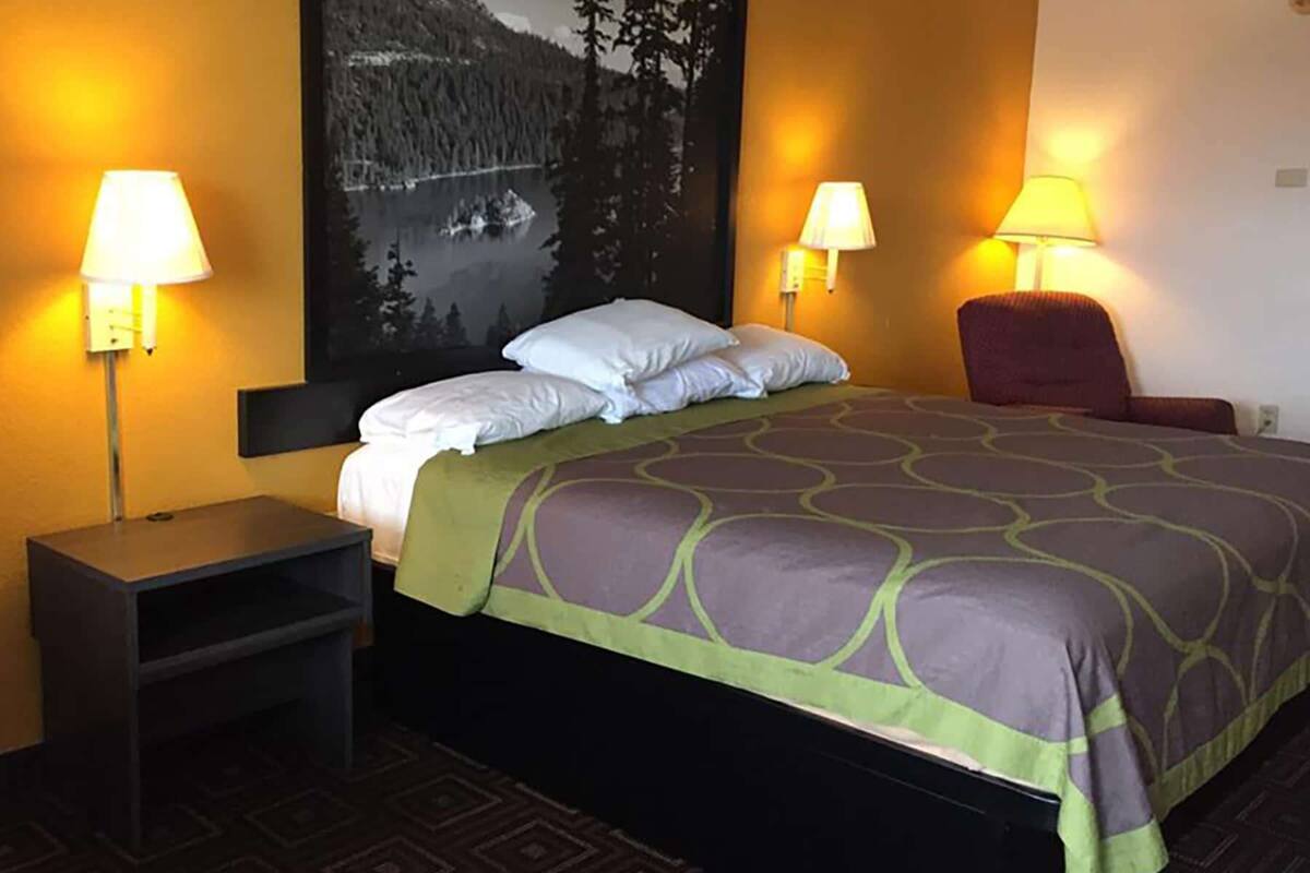 Ein Hotelzimmer mit einem Bett, zwei Nachttischlampen, einem Sessel, einem kleinen Tisch und einem großen Gemälde an der Wand.