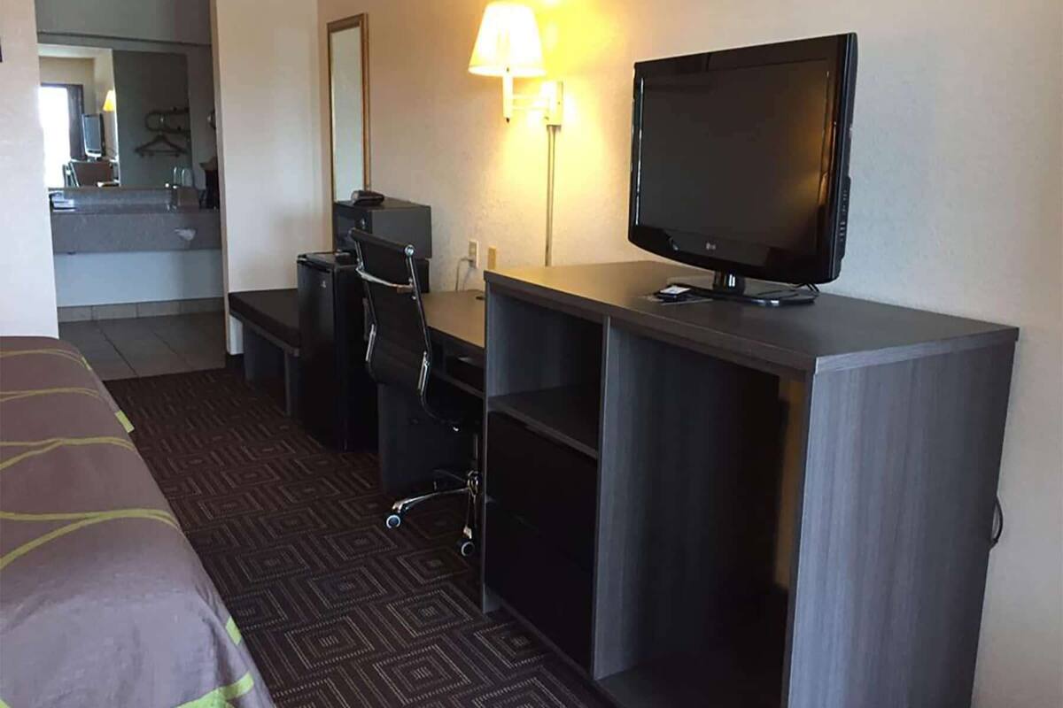 Ein Hotelzimmer mit einem Bett, einem Schreibtisch mit Computer und Fernseher, einem Sessel und einer Lampe.