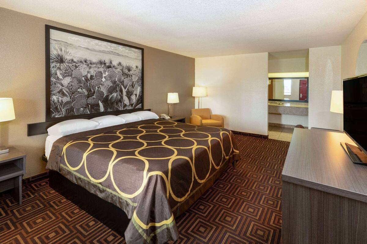 Ein Hotelzimmer mit einem großen Bett, einem Schreibtisch, einem Sessel, einem Fernseher und einem Gemälde an der Wand.