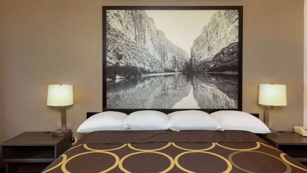 Une chambre d’hôtel avec un grand lit, deux tables de chevet, une petite table, une lampe fixée au mur et un tableau représentant un canyon.