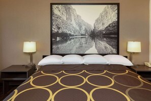 Une chambre d’hôtel avec un grand lit, deux tables de chevet, une petite table, une lampe fixée au mur et un tableau représentant un canyon.