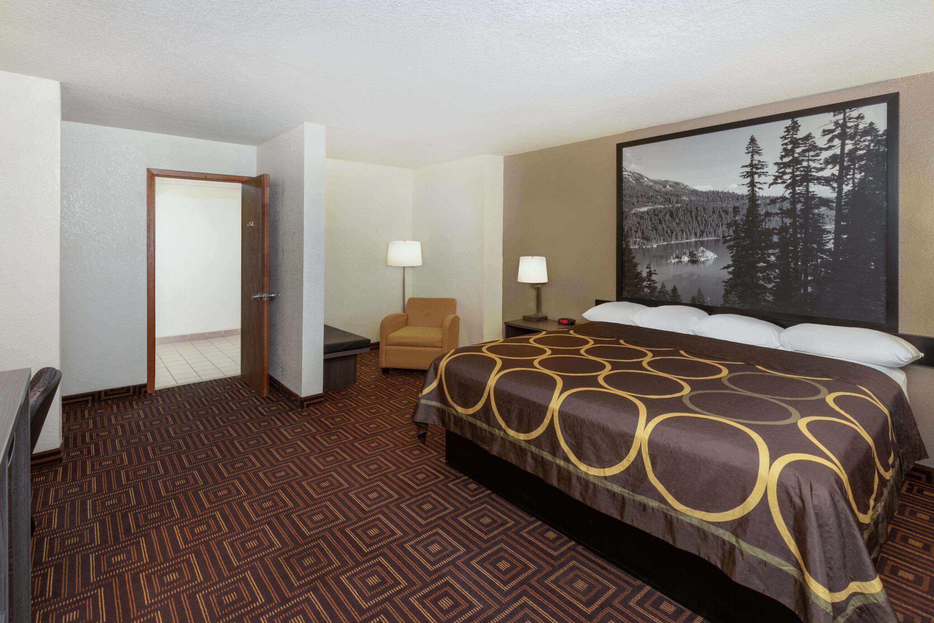 A hotel room with a large bed, a chair, a desk, and a nightstand.