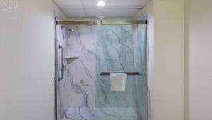 Une douche fermée par des parois de verre, avec un mur décoré de motifs en marbre et un porte-serviettes.