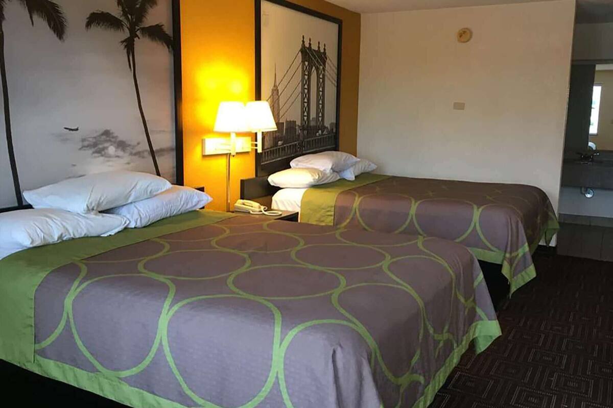 Ein Hotelzimmer mit zwei Betten, einem Nachttisch, einer Lampe und einem Bild einer Brücke.