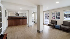 A reception area with a wooden reception desk, a clock, and two armchairs. - Townhouse Inn (High Point)