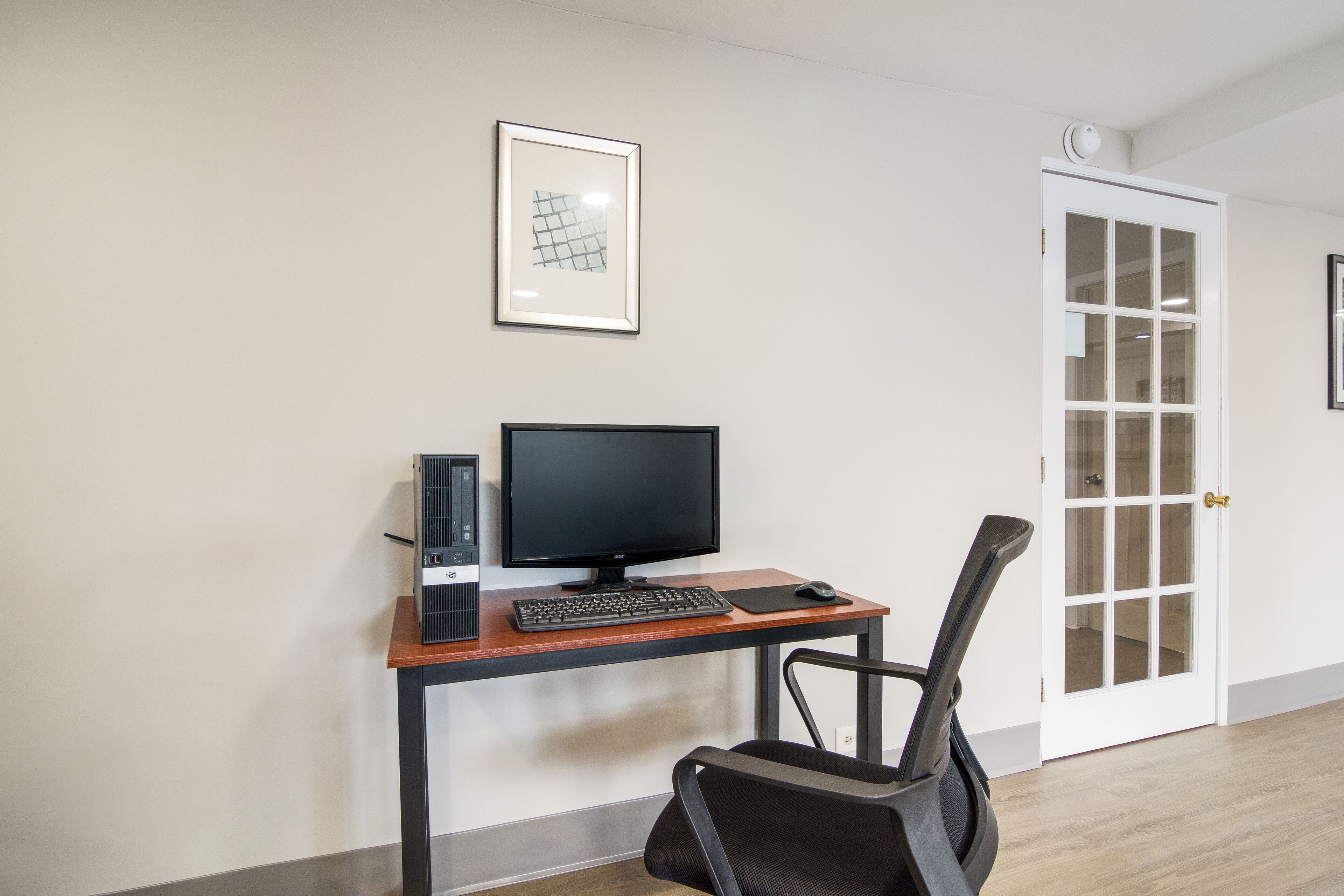 A room with a wooden desk, a computer, a chair, and a door with glass panels.