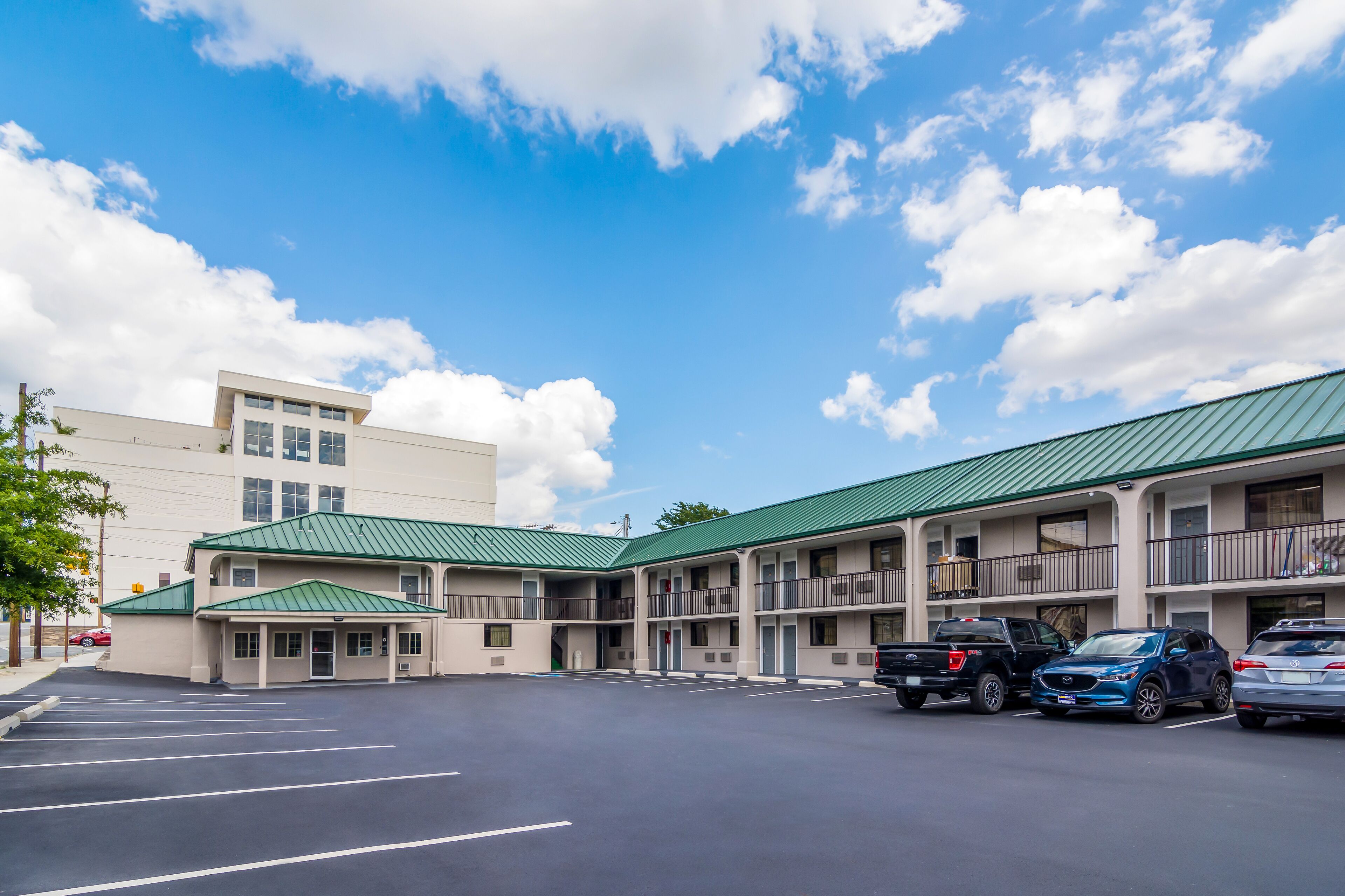 A motel with a green roof, multiple balconies, and a parking lot with several cars.